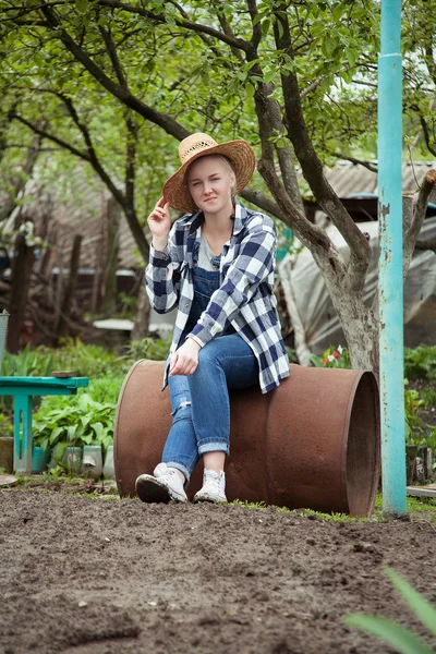 Cowgirl sitting on a rustic iron barrel in the garden