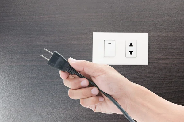 Hand holding  plug and socket on wall