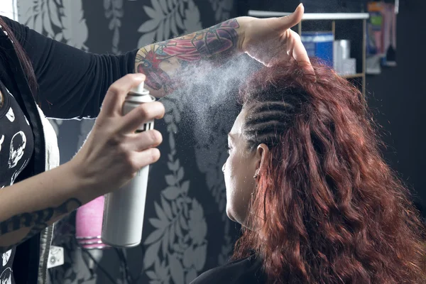 Hairdresser with hair spray fixating one customer's hair.