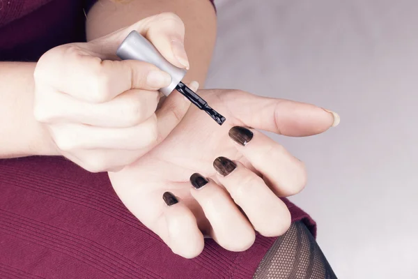 Woman polish her nails with black nail polish