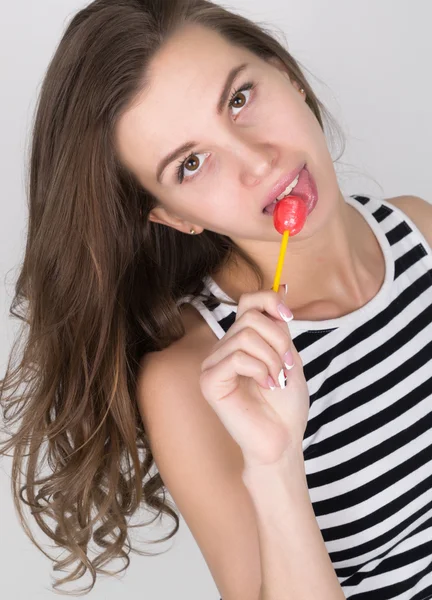 Beautiful slim girl in black shorts and a striped top, eating candy. closeup lip licking candy