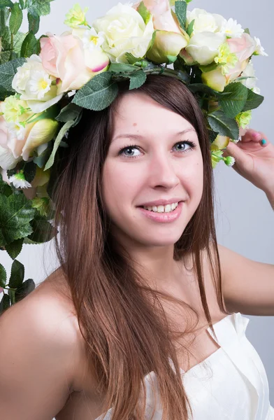 Beautiful young leggy blonde in a little white dress on a swing, wooden swing suspended from a rope hemp, rope wrapped vine and ivy. girl with floral wreath on her head. spring mood