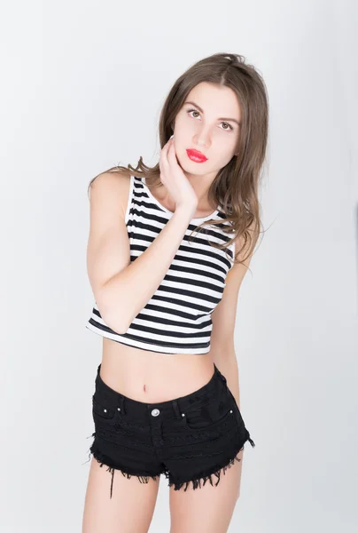 Close-up beautiful slim woman in black shorts and a striped top is in multi-colored shoes, brunette posing