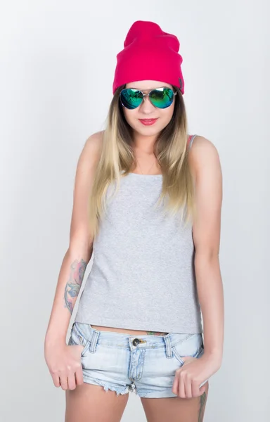 Teenager girl in denim shorts and a gray T-shirt and a pink knit hat, tied at the hips plaid shirt. girl in sunglasses