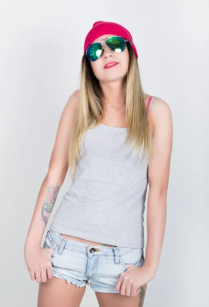 Teenager girl in denim shorts and a gray T-shirt and a pink knit hat, tied at the hips plaid shirt. girl in sunglasses