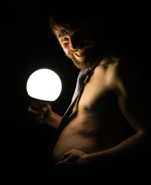 Bearded man with a large belly in a tie on a naked body holding a large lamp