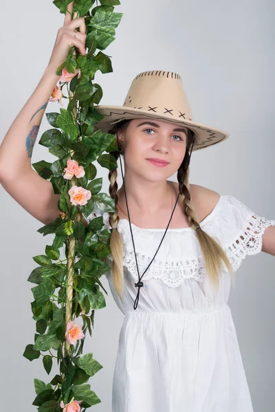 Beautiful young leggy blonde in a little white dress and white cowboy hat on a swing, wooden swing suspended from a rope hemp, rope wrapped vine and ivy. she clinging to the vine.