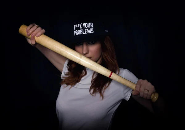 Young teenager girl in a white shirt and black cap, posing with a baseball bat. play of light and shadows