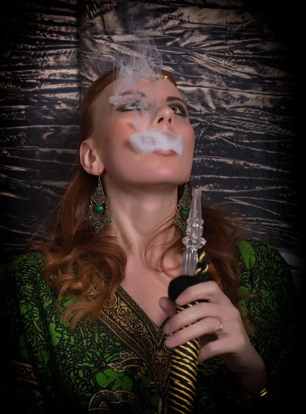 Close-up portrait of a elegant young redhead woman, with oriental make-up and shawl over her head bright red lips, smokes a hookah