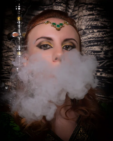 Close-up portrait of a elegant young redhead woman, with oriental make-up and shawl over her head bright red lips, smokes a hookah