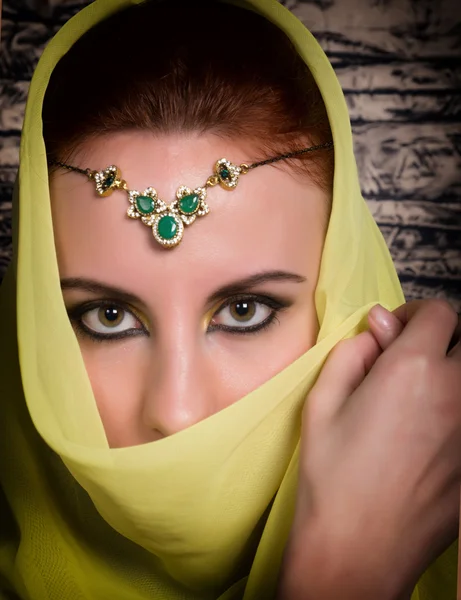 Closeup of beautiful young woman with oriental make-up and shawl over her head. caucasian woman dressed in oriental style. Professional makeup
