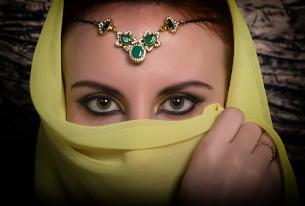 Closeup of beautiful young woman with oriental make-up and shawl over her head. caucasian woman dressed in oriental style. Professional makeup