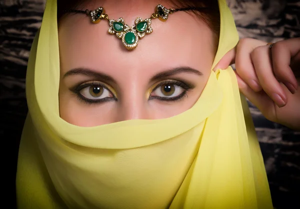 Closeup of beautiful young woman with oriental make-up and shawl over her head. caucasian woman dressed in oriental style. Professional makeup