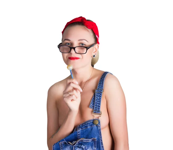 Beautiful young leggy blondy girl in a red bandana, denim overalls over his naked body, licking candy