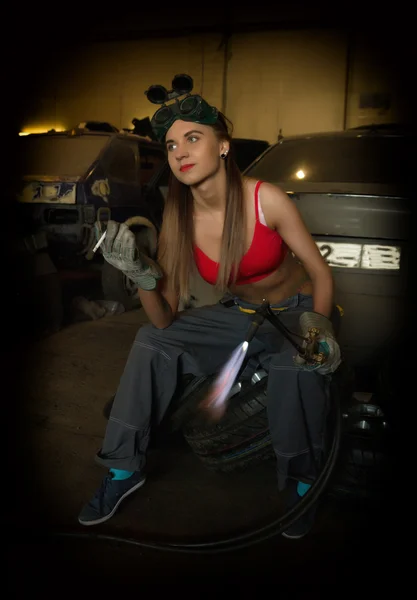 Girl mechanic sitting on a tire with blowpipe smoking in a garage