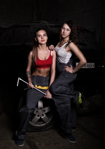 Sexy girls mechanic sitting on a tire holding a wrench in his hand on a car repairs. colorless life concept