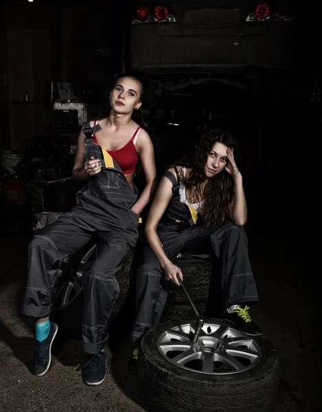 Tired mechanics sexy girls sitting on a pile of tires on a car repairs and smoke, one of the girls holding a wrench in his hand. colorless life concept