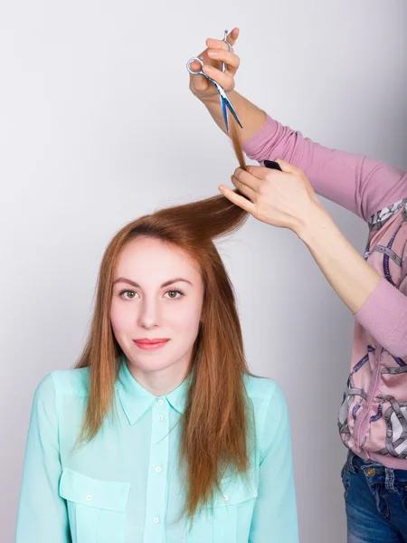 Beautiful young redhaired model in salon, hairdresser does a hairstyle. trims the hair tips with scissors