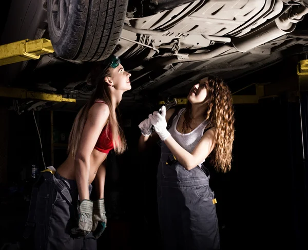 Beautiful young female mechanic inspecting car in auto repair shop. Sexy mechanic