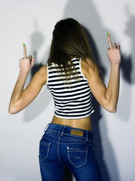 Sexy blonde girl in jeans and striped t-shirt, turned his back and raised both hands up, showing middle finger