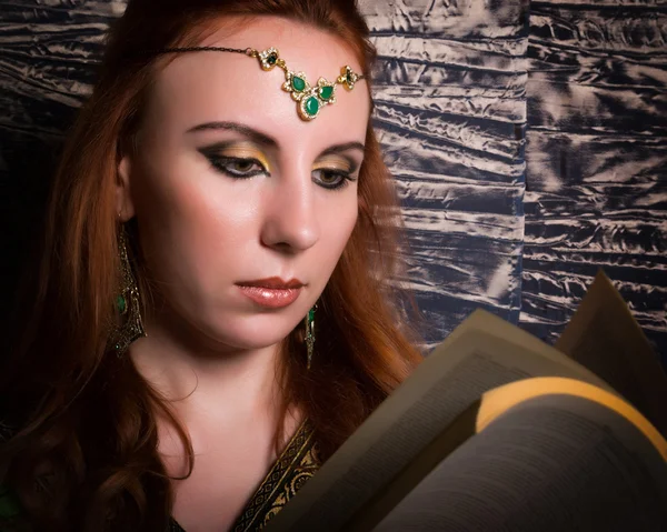 Closeup of Beautiful woman dressed in oriental style with oriental patterns on the hands and face, reading a thick book