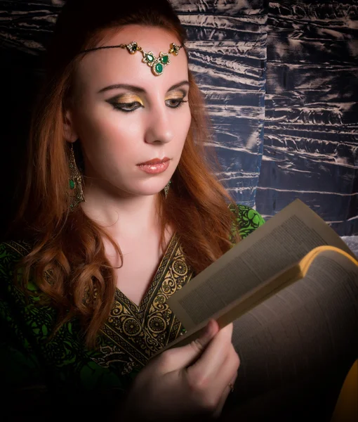 Closeup of Beautiful woman dressed in oriental style with oriental patterns on the hands and face, reading a thick book