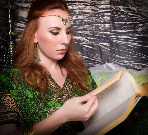 Closeup of Beautiful woman dressed in oriental style with oriental patterns on the hands and face, reading a thick book
