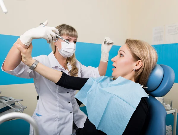 Doctor examines the oral cavity on tooth decay. Caries protection. Tooth decay treatment. Doctor puts injection to the patient, patient holds the doctors hand and does not put a shot