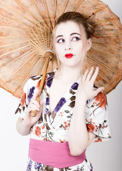 Beautiful girl dressed as a geisha girl holding a Chinese umbrella. Geisha makeup and hair dressed in a kimono. The concept of traditional Japanese values