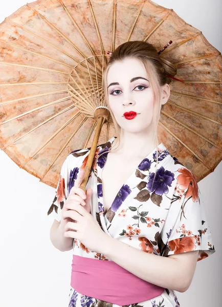 Beautiful girl dressed as a geisha girl holding a Chinese umbrella. Geisha makeup and hair dressed in a kimono. The concept of traditional Japanese values
