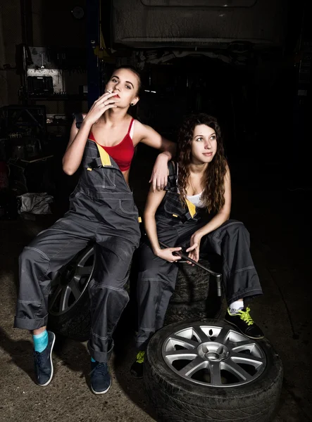 Tired mechanics sexy girls sitting on a pile of tires on a car repairs, one of the girls smoke. colorless life concept