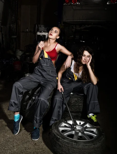 Tired mechanics sexy girls sitting on a pile of tires on a car repairs, one of the girls smoke. colorless life concept
