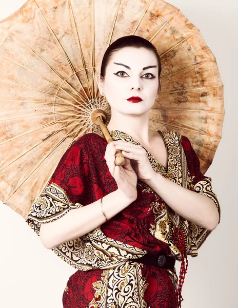 Beautiful girl dressed as a geisha girl holding a Chinese umbrella. Geisha makeup and hair dressed in a kimono. The concept of traditional Japanese values