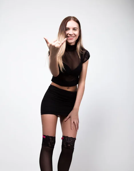 Young fashion woman in high heels, studio shot. woman in a short black skirt and a transparent top showing Shaka sign