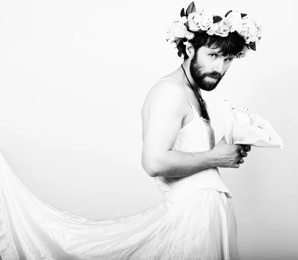 Bearded man in a womans wedding dress on her naked body, holding a flower. on his head a wreath of flowers. funny bearded bride, black and white