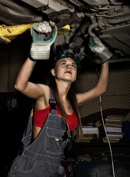 Beautiful young female mechanic inspecting car in auto repair shop. Sexy mechanic