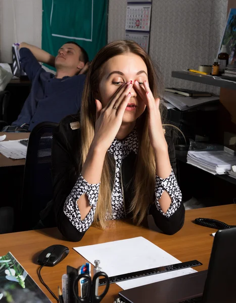 Beautiful office female worker in panic holding his head. on a background sleeping colleagues. office concept