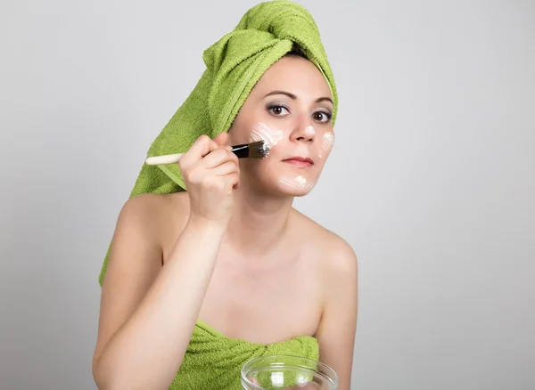 Beautiful Young woman dressed in a bath towel makes a cosmetic mask on the face. beauty industry and home skin care concept