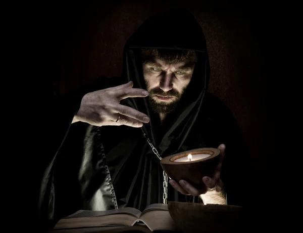 Necromancer casts spells from thick ancient book by candlelight on a dark background