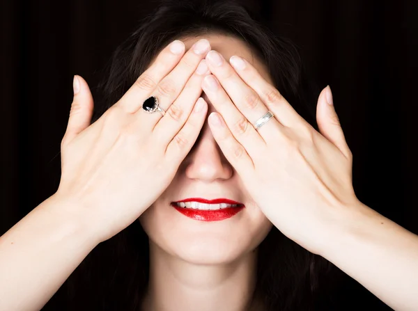 Close-up woman looks straight into the camera on a black background. laughing woman covering her eyes with her hand. expresses different emotions