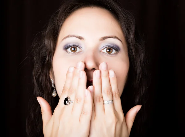 Close-up woman looks straight into the camera on a black background. She covered her mouth with her hand. expresses different emotions