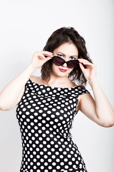 Beautiful young woman removes sun glasses, wears a dress with polka dots