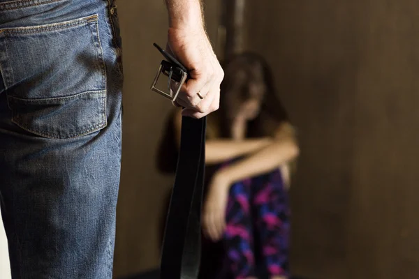 Frightened woman sitting in the corner with a faceless man holding a belt, a conceptual shoot portraying the process and effects of domestic violence