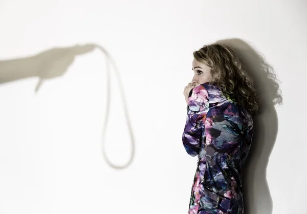 Frightened woman standing near the wall with a faceless man holding a belt, a conceptual shoot portraying the process and effects of domestic violence