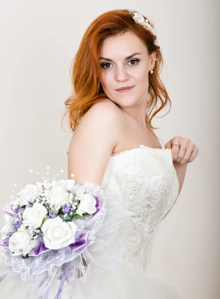 Red-haired bride in a wedding dress holding wedding bouquet, bright unusual appearance. Beautiful wedding hairstyle and bright make-up