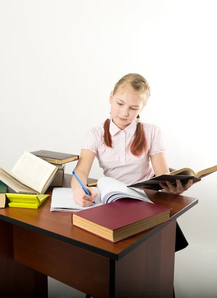 Teenager girl sitting at a table in front of her large pile of books. schoolgirl reading a book and doing homework