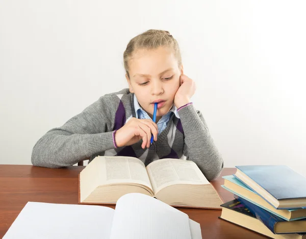 Teenager girl sitting at a table in front of her large pile of books. schoolgirl reading a book and doing homework