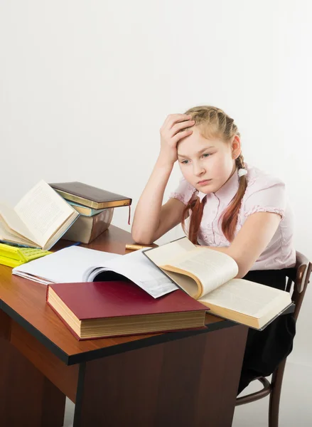 Teenager girl sitting at a table in front of her large pile of books. schoolgirl reading a book and doing homework