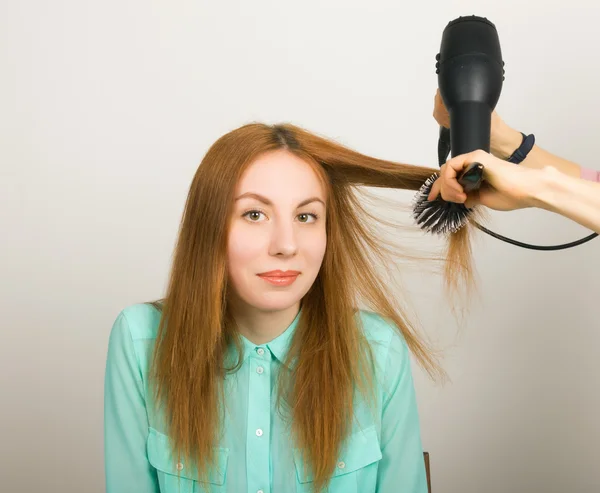 Beautiful young red-haired girl at the hairdresser makes blow drying, shorn bangs, hair polishing