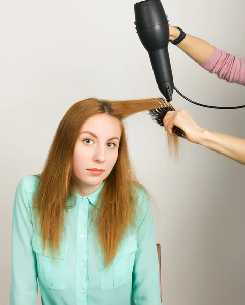 Beautiful young red-haired girl at the hairdresser makes blow drying, shorn bangs, hair polishing
